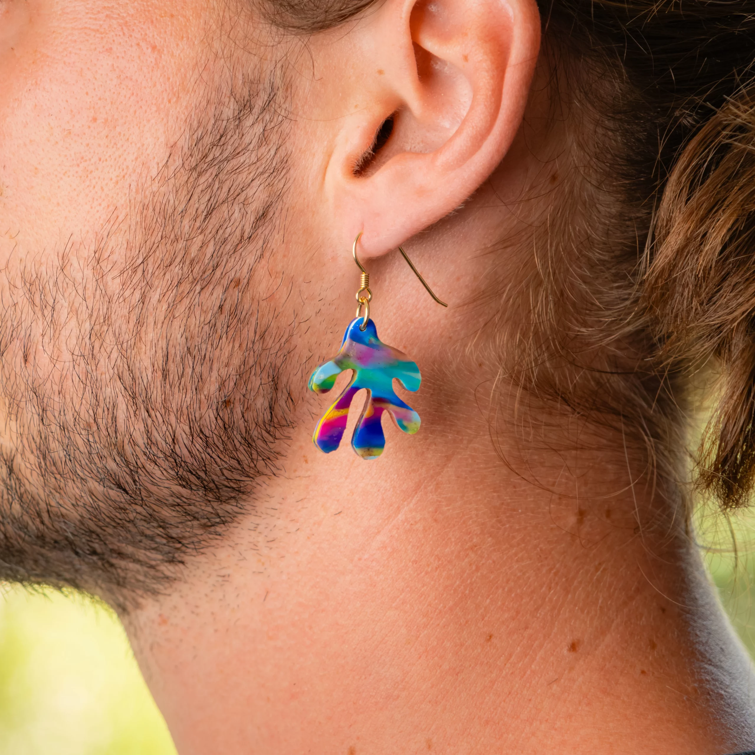 Homme portant la boucle d'oreille recyclée Coralia de Sauvage Méditerranée, collection Les Beaux Jours, coloris Bleu Jaune Violet/Rose.