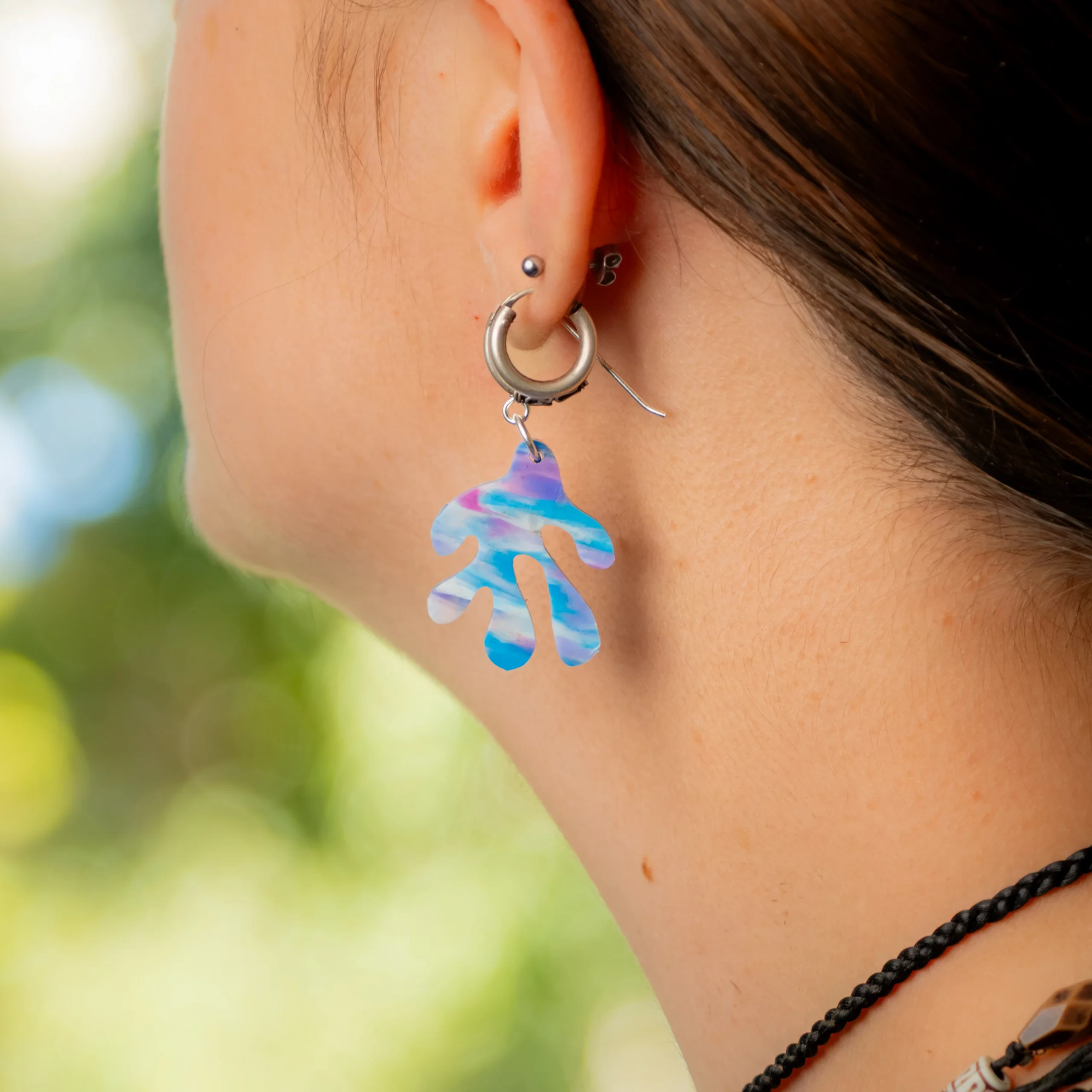 Femme portant la boucle d'oreille recyclée Coralia de Sauvage Méditerranée, collection Les Beaux Jours, coloris Bleu Violet/Rose Blanc.