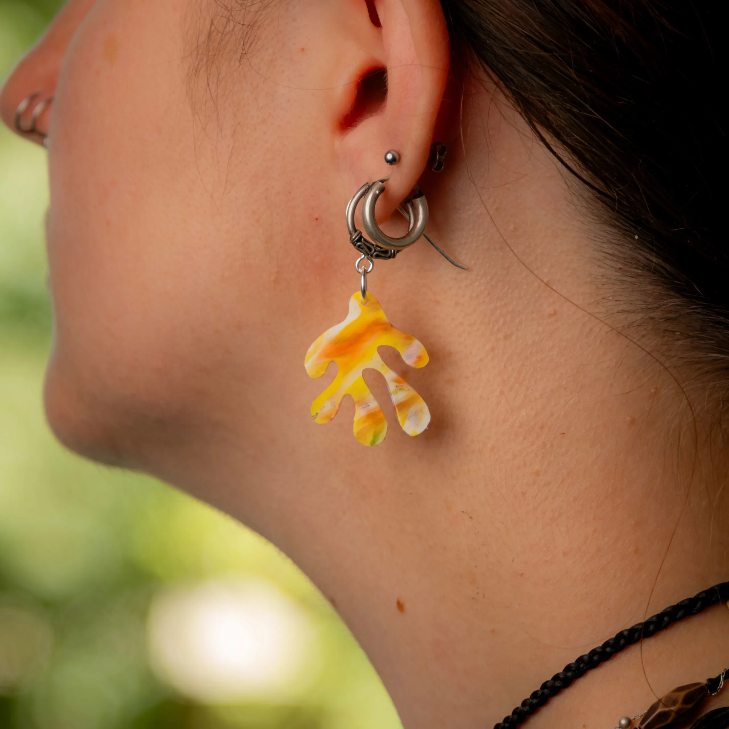 Femme portant la boucle d'oreille recyclée Coralia de Sauvage Méditerranée, collection Les Beaux Jours, coloris Jaune Orange Blanc.