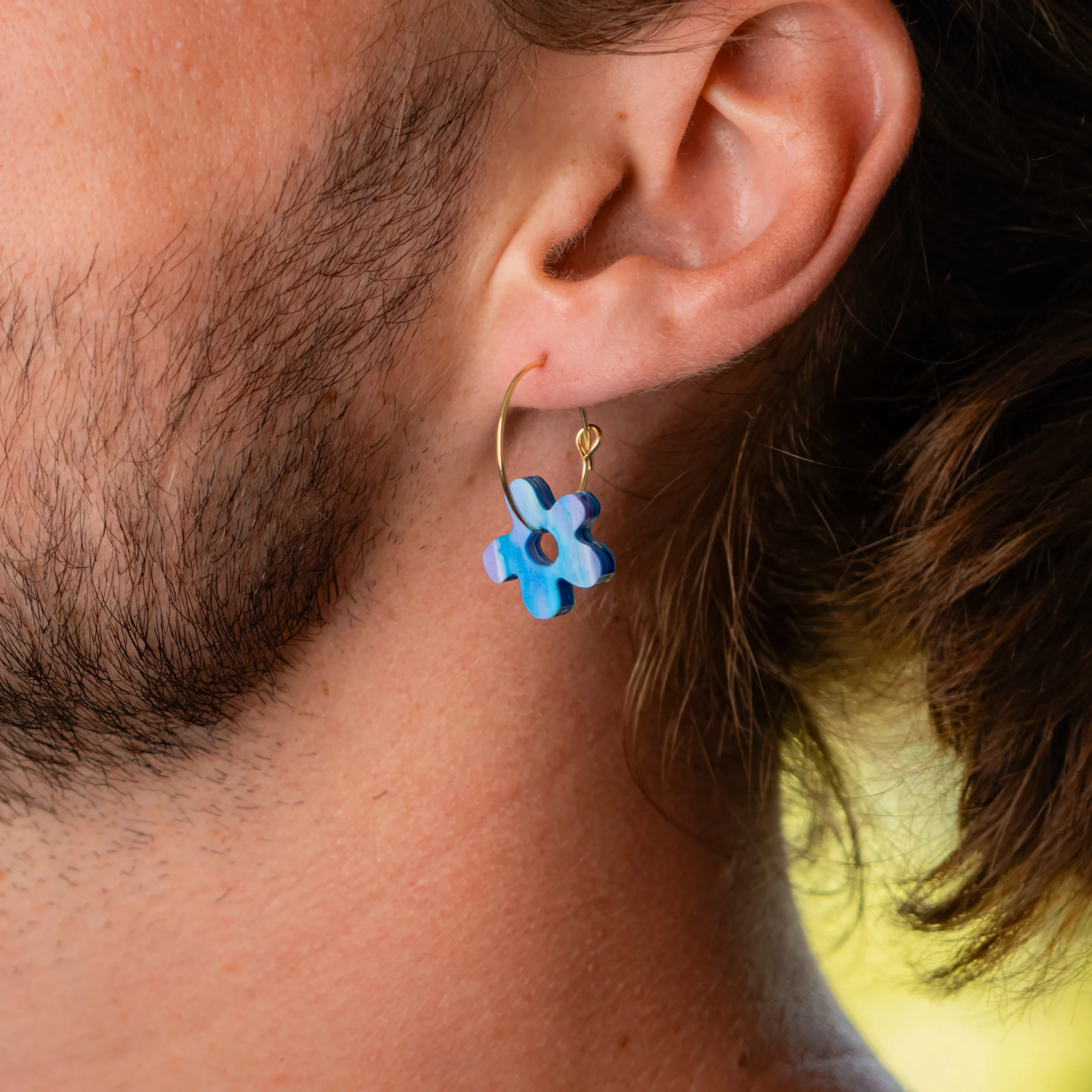 Homme portant la boucle d'oreille recyclée Fleur de Sauvage Méditerranée, collection Les Beaux Jours, coloris Bleu Violet/Rose Blanc.