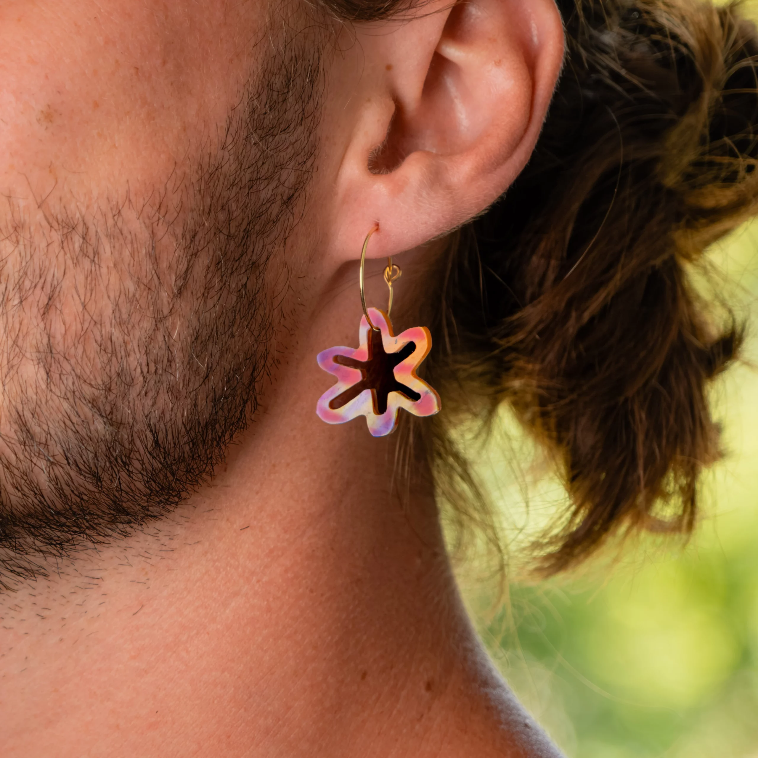 Homme portant la boucle d'oreille recyclée Gazania de Sauvage Méditerranée, collection Les Beaux Jours, coloris Violet/Rose Jaune Orange.