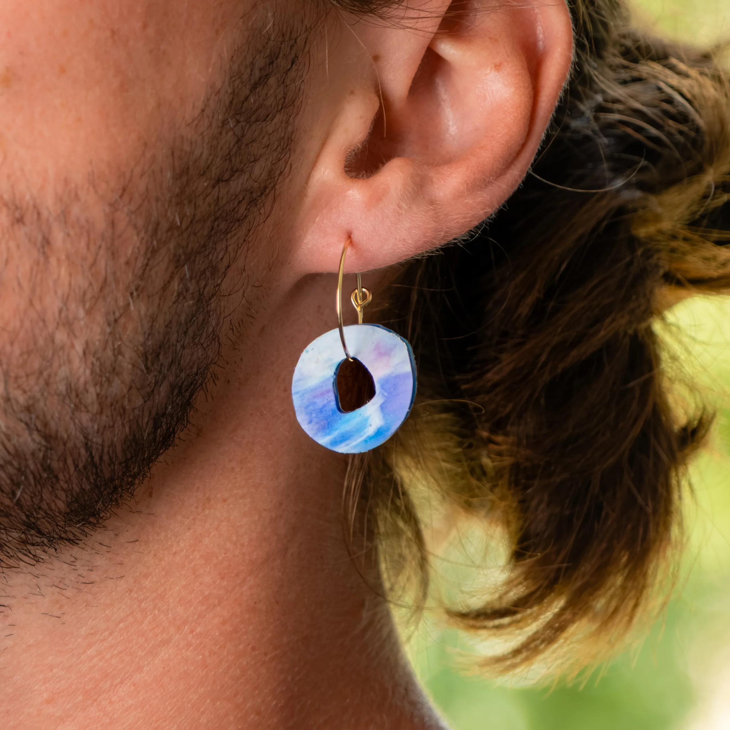Homme portant la boucle d'oreille recyclée Halo de Sauvage Méditerranée, collection Les Beaux Jours, coloris Bleu Violet/Rose Blanc.