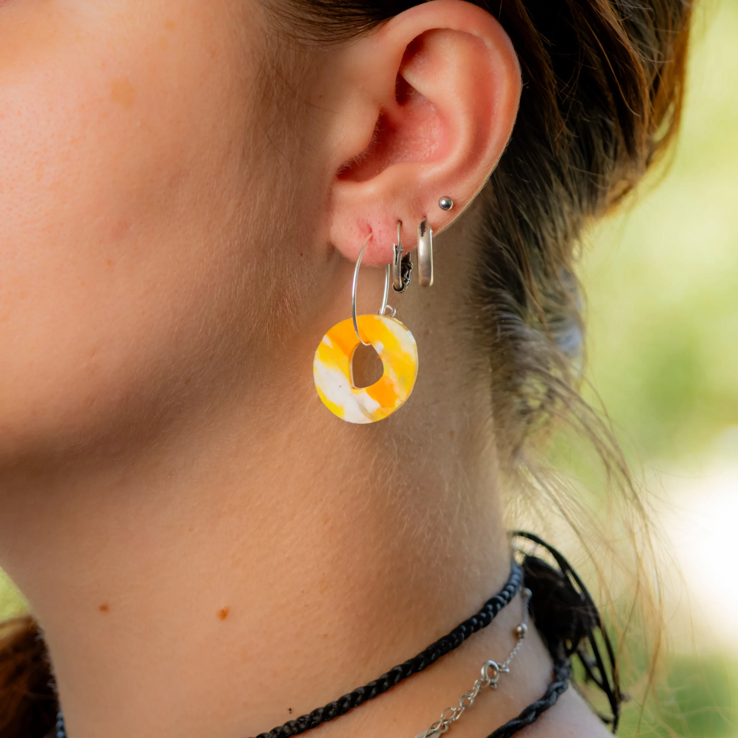 Femme portant la boucle d'oreille recyclée Halo de Sauvage Méditerranée, collection Les Beaux Jours, coloris Jaune Orange Blanc.