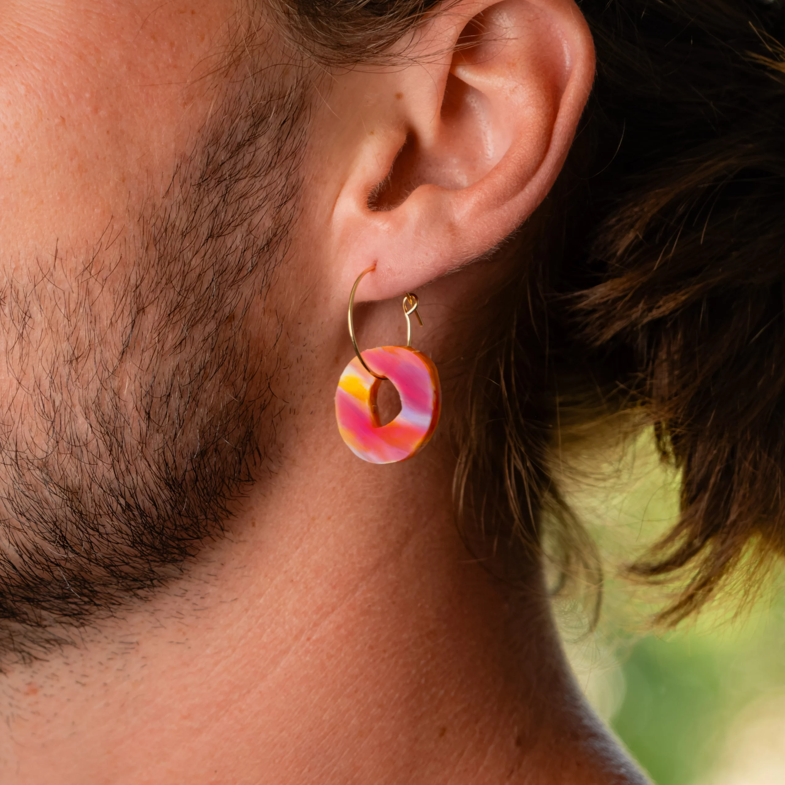 Homme portant la boucle d'oreille recyclée Halo de Sauvage Méditerranée, collection Les Beaux Jours, coloris Violet/Rose Jaune Orange.