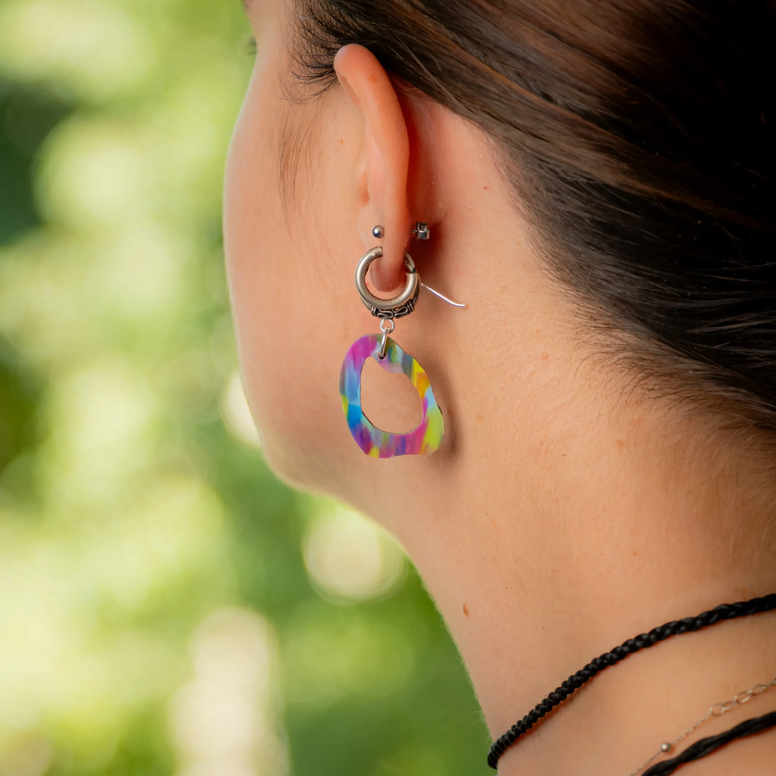 Femme portant la boucle d'oreille recyclée Lagune de Sauvage Méditerranée, collection Les Beaux Jours, coloris Bleu Jaune Violet/Rose.