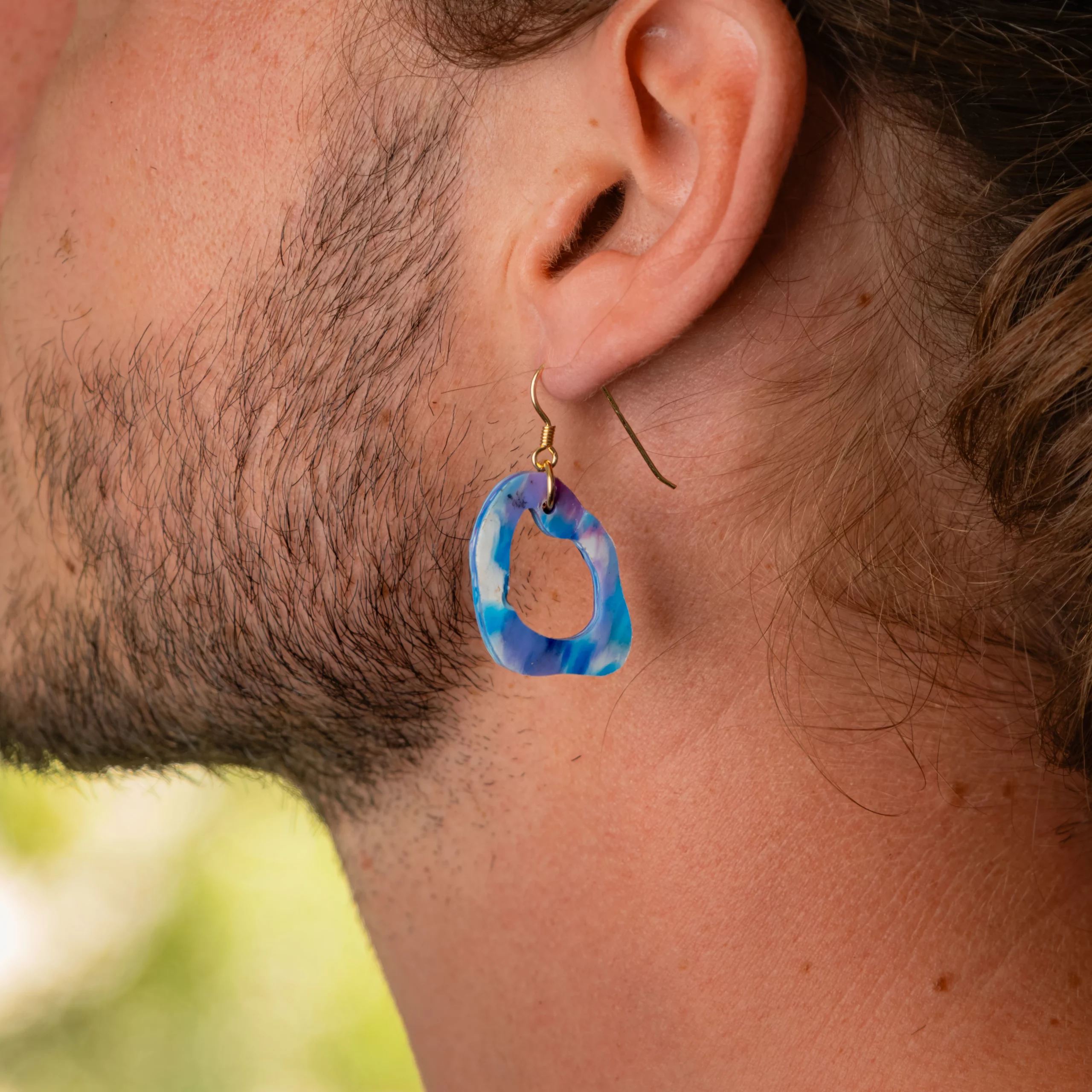Homme portant la boucle d'oreille recyclée Lagune de Sauvage Méditerranée, collection Les Beaux Jours, coloris Bleu Violet/Rose Blanc.