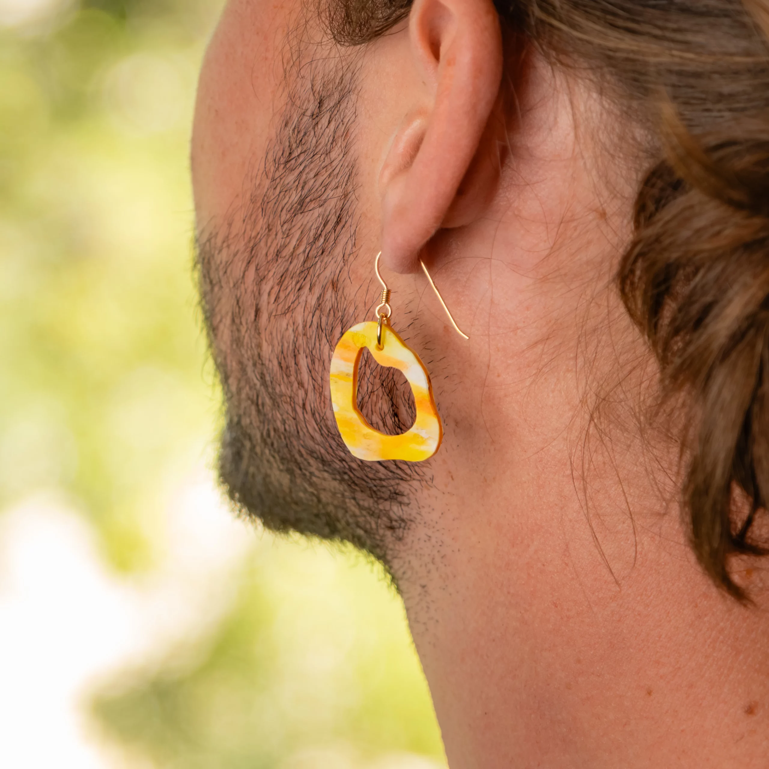 Homme portant la boucle d'oreille recyclée Lagune de Sauvage Méditerranée, collection Les Beaux Jours, coloris Jaune Orange Blanc.