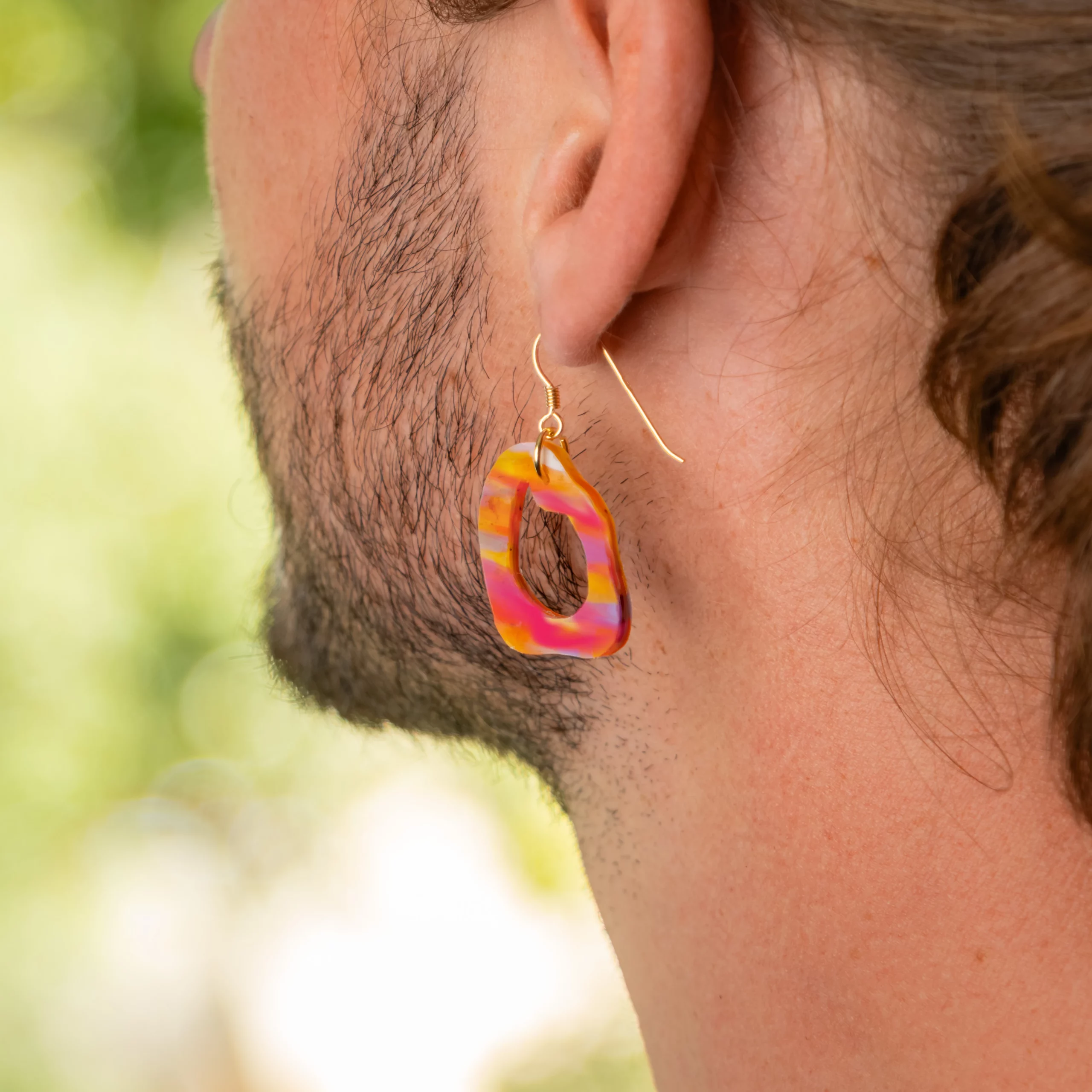 Homme portant la boucle d'oreille recyclée Lagune de Sauvage Méditerranée, collection Les Beaux Jours, coloris Violet/Rose Jaune Orange.