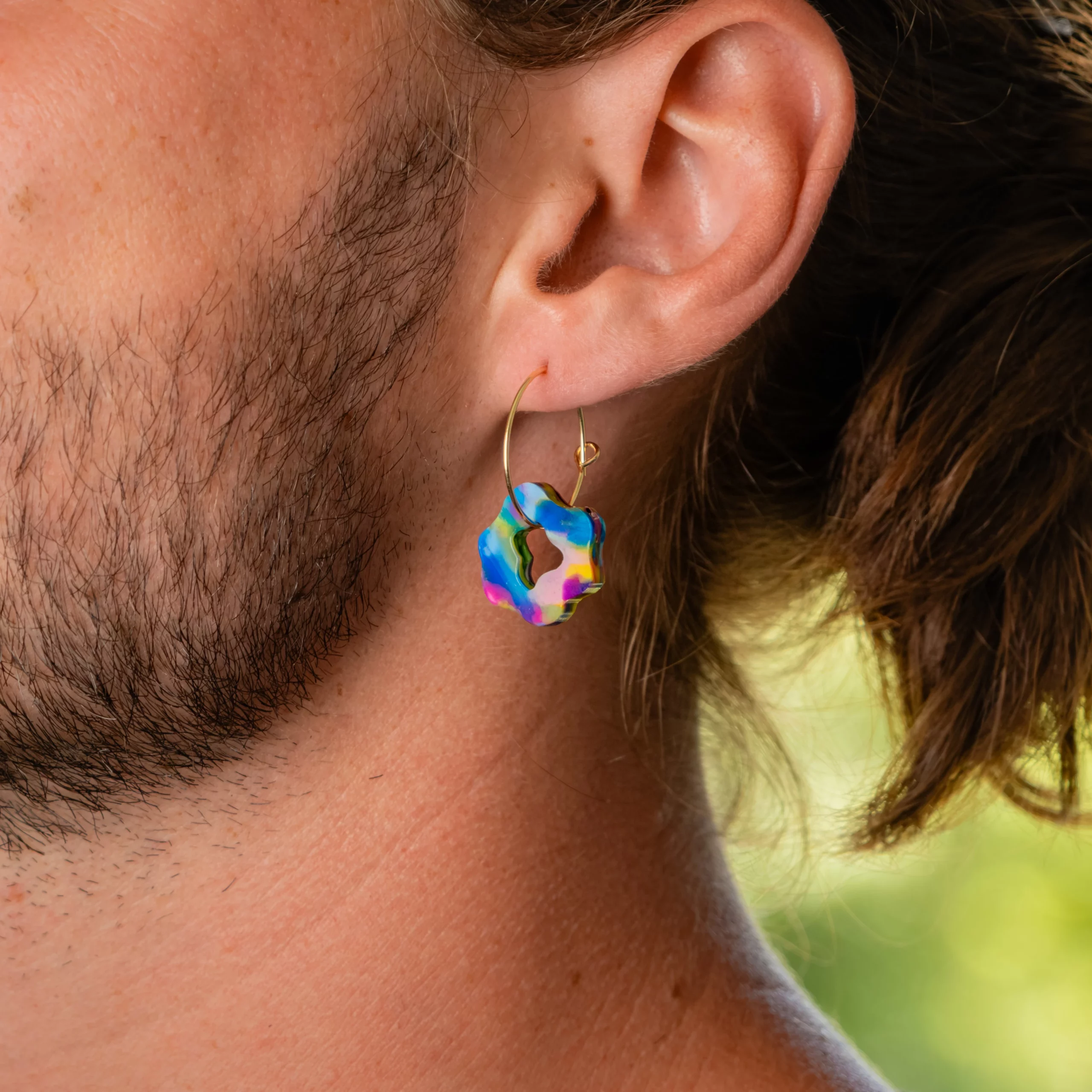 Homme portant la boucle d'oreille recyclée Pétale de Sauvage Méditerranée, collection Les Beaux Jours, coloris Bleu Jaune Violet/Rose.