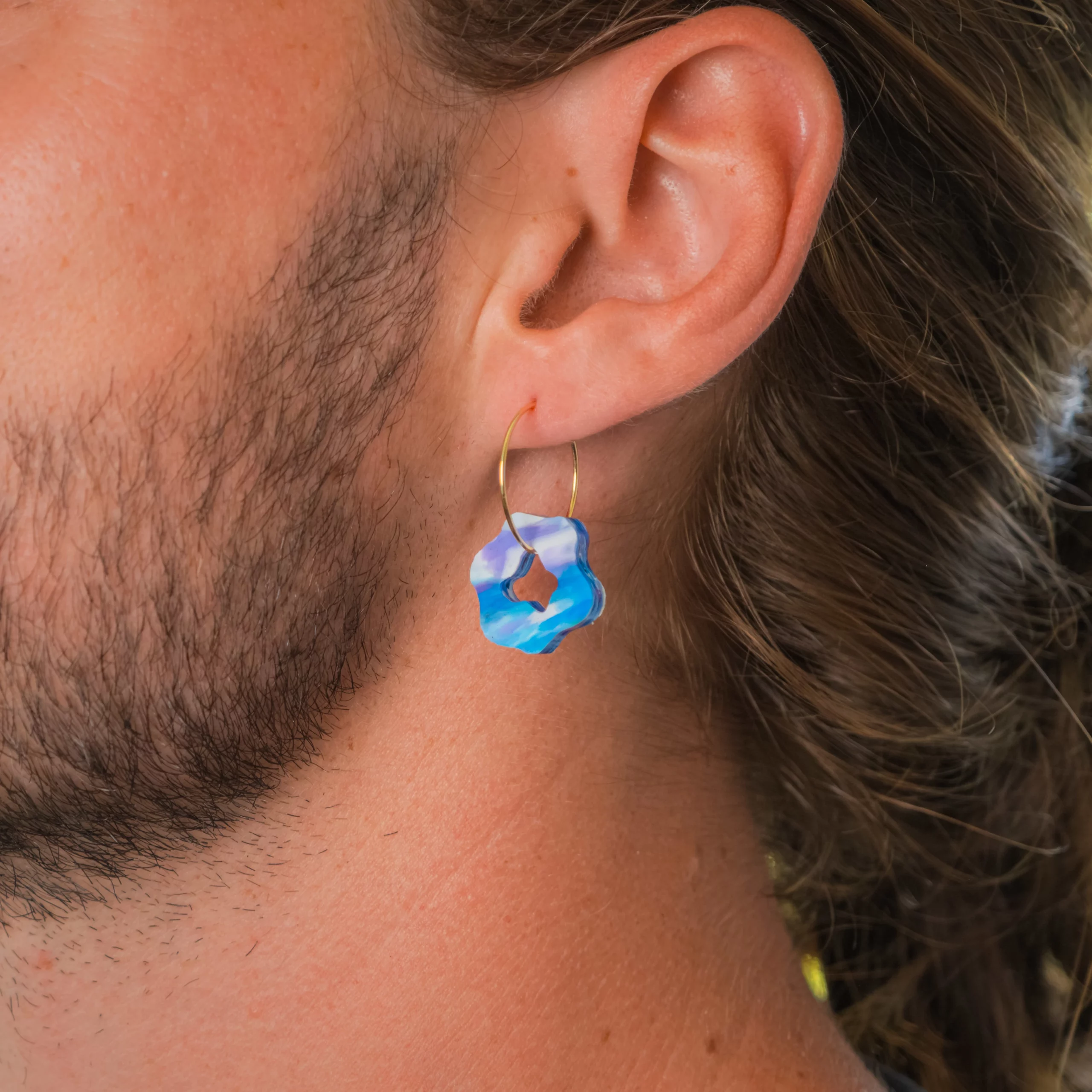 Homme portant la boucle d'oreille recyclée Pétale de Sauvage Méditerranée, collection Les Beaux Jours, coloris Bleu Violet/Rose Blanc.